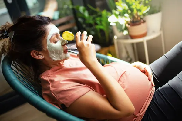 Pregnant woman relaxing on a spa bed while receiving a gentle facial treatment from a skincare specialist in a calm, professional clinic setting.