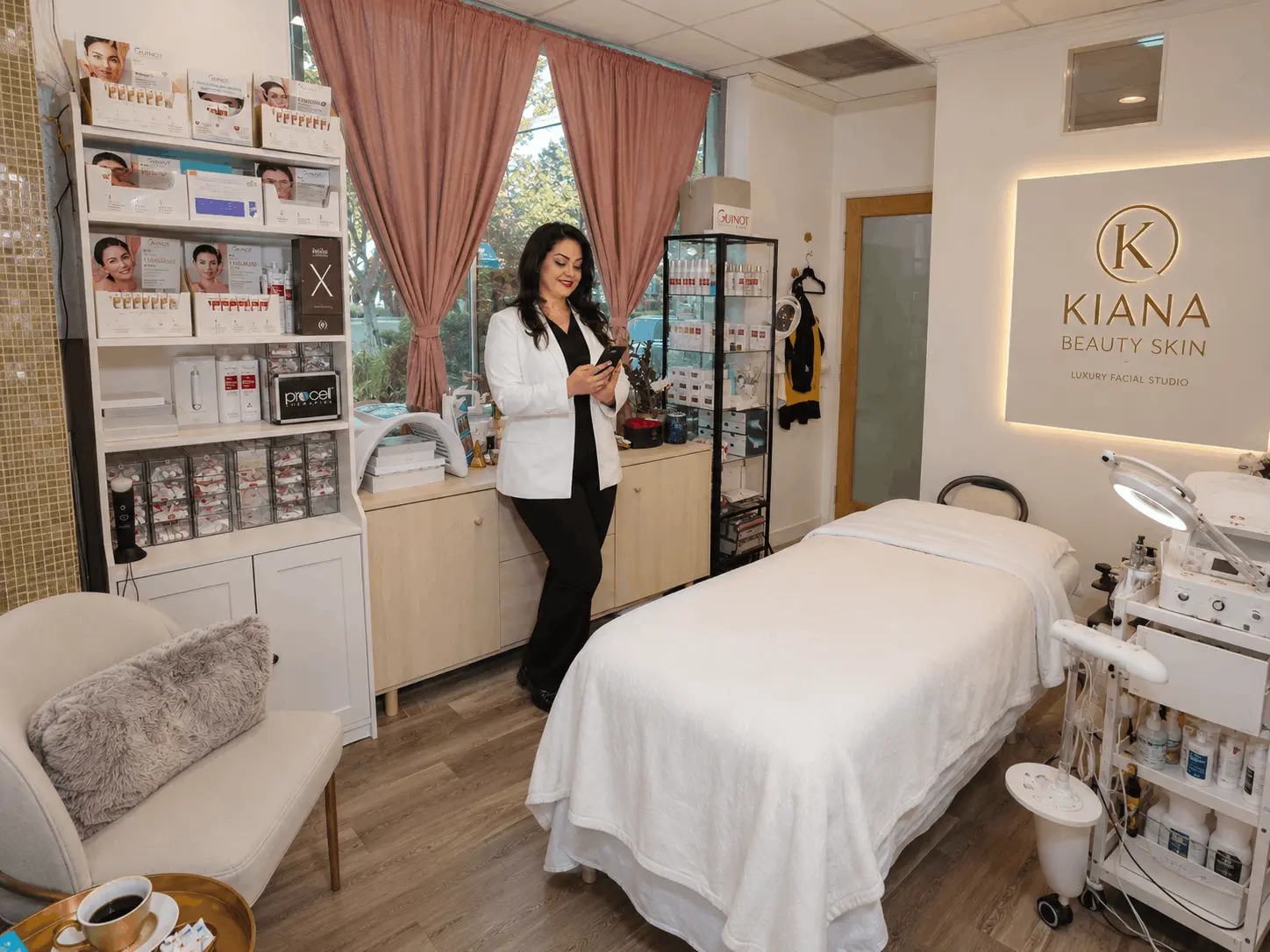 Kiana inside her private facial studio in Aliso Viejo, featuring a facial treatment bed, professional skincare equipment, and Guinot products.
